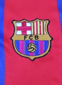 Buy Soccer Kits in Bulk 8 Close-up of official logo and patches on FCB Jersey Messi 10: "Close-up of official Barcelona logo and patches on FCB Jersey Messi 10 for an authentic fan experience.