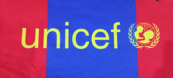 Close-up of official logo and patches on FCB Jersey Messi 10: "Close-up of official Barcelona logo and patches on FCB Jersey Messi 10 for an authentic fan experience.